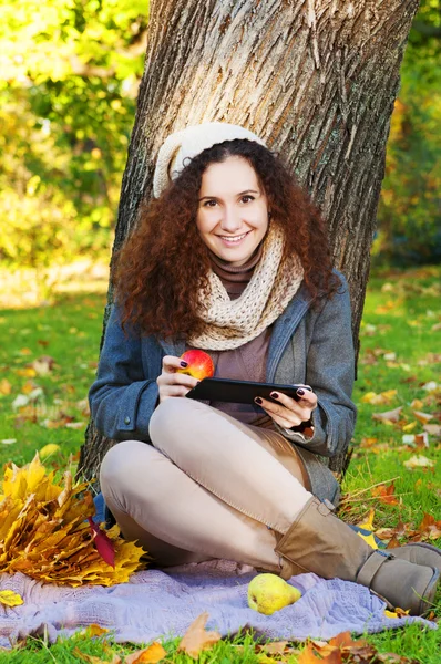 Mulher bonita e elegante sentada com tablet e maçã em um parque no outono — Fotografia de Stock