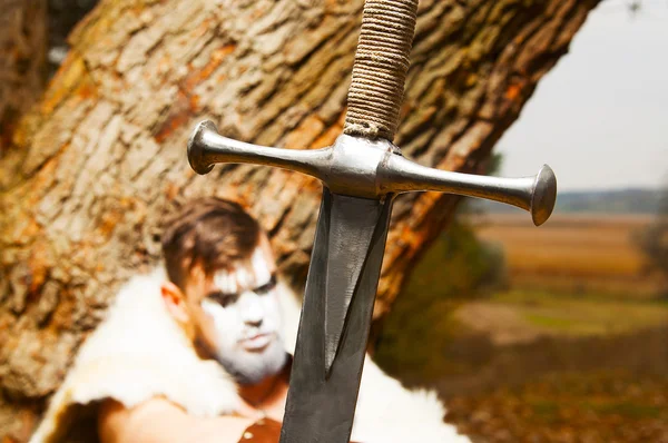 Retrato de um antigo guerreiro musculoso. Espada em primeiro plano — Fotografia de Stock