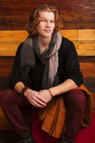 Красивый молодой человек, сидящий на чемодане на деревянном фоне — стоковое фото