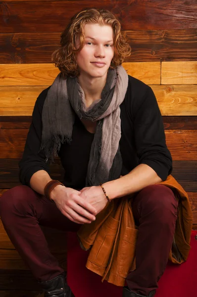 Handsome young man sitting on the suitcase on the wooden background — Stock Photo, Image