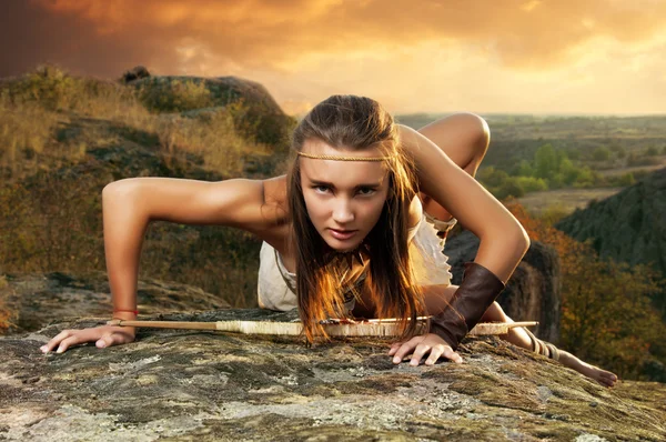 Mujer primitiva en una roca al atardecer. Mujer amazona Imagen de stock