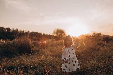 Küçük kız gün batımında bir yaz tarlasında yürüyor.