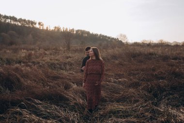 Güzel, genç, hamile, mutlu çift sonbahar tarlasında yürüyor.