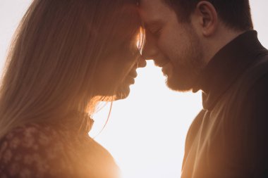 Gün batımında dağda poz veren sevimli genç bir çift. Erkek arkadaşı kız arkadaşını alnından öpüyor, hipster, açık hava portresi, yakın plan portresi. Kesilmiş fotoğraf.