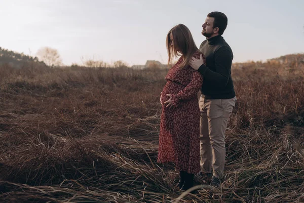 美丽的孕妇和她的丈夫抱着肚子在大自然的背景下 秋天的风景 — 图库照片