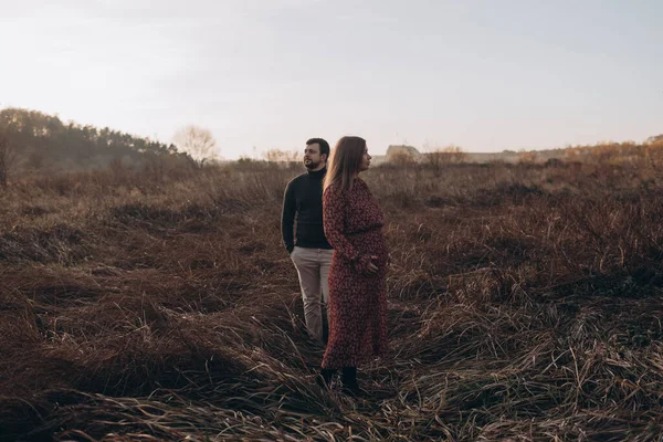美しい妊娠中の女性と彼女の夫は 自然の背景に腹を抱いて 秋の風景 — ストック写真