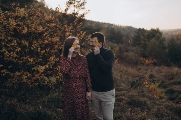 美丽的怀孕的年轻貌美的夫妇在秋天的田野里散步 — 图库照片