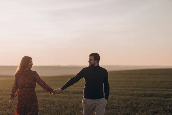 夫と妊娠中の妻は外の畑で日没時に歩いている — ストック写真