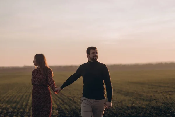 夫と妊娠中の妻は外の畑で日没時に歩いている — ストック写真