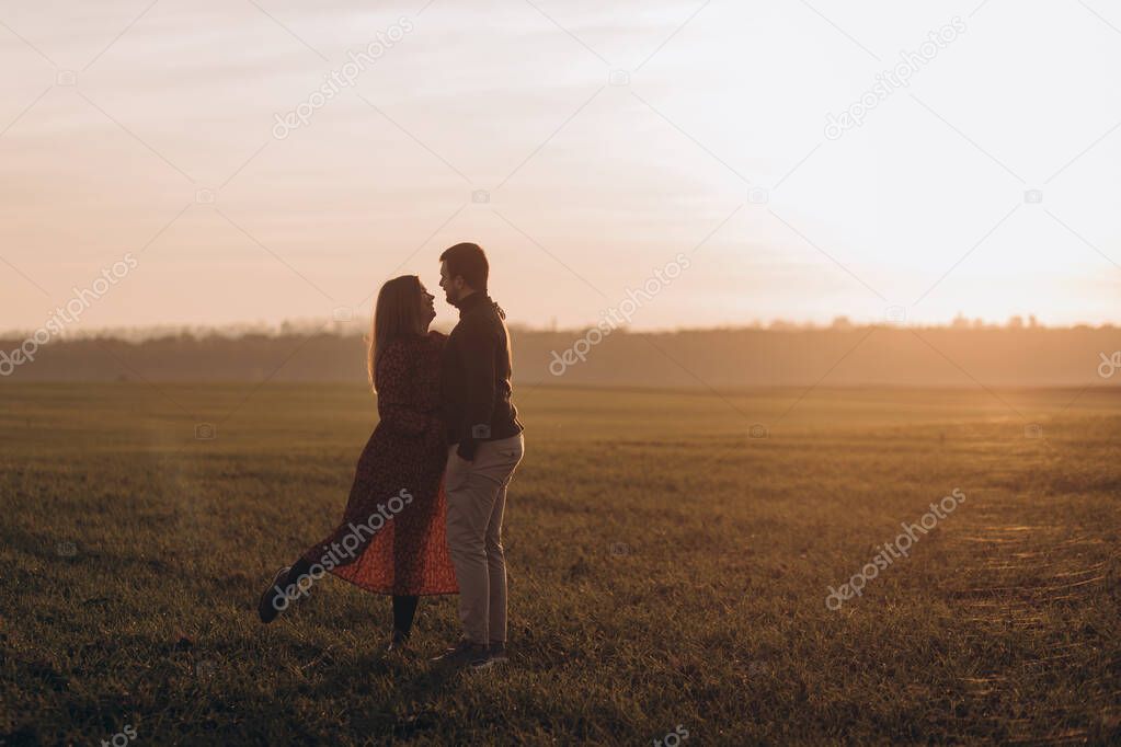 Husband and his pregnant wife are walking at sunset in field on the outside