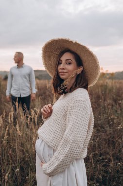 Kocasıyla hamile karısı gün batımında dışarıda yürüyorlar. Açık havada romantik hamilelik.