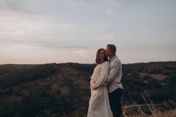 幸せな若い妊娠中のカップルキスで山の上で 背景に澄んだ空 — ストック写真