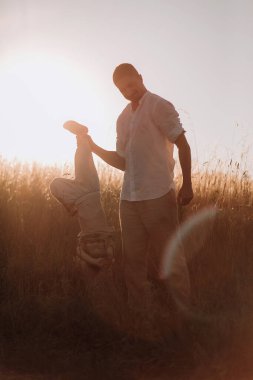 Küçük çocuk yazın gün batımında tarlada babasıyla oynuyor. 