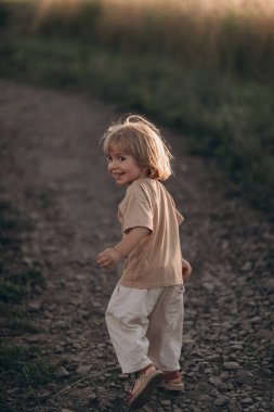 Küçük çocuk yazın gün batımında tarlada oynuyor. 
