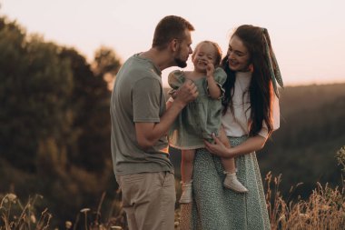 Mutlu aile gün batımında parkta yürür. Anne, baba ve bebek. Sağlıklı aile sahada oynar. Mutlu aile kavramı
