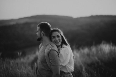 Genç mutlu çift gün batımı dağlarında sarılıp el ele tutuşuyorlar.