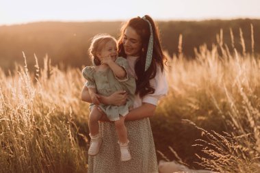 Mutlu anne ve küçük kızı gün batımı dağlarında yürümenin keyfini çıkarın.