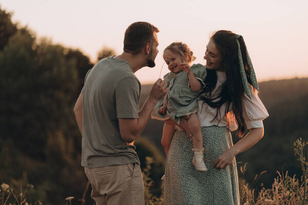 Happy family walks in park at sunset. Mom, dad and baby. Healthy family plays in field. Happy family concept