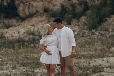 Hamile kadın ve kocası açık havada karnına sarılıyorlar.