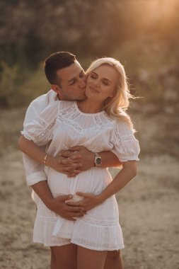 Hamile kadın ve kocası açık havada karnına sarılıyorlar.