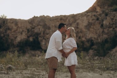 Hamile kadın ve kocası açık havada karnına sarılıyorlar.