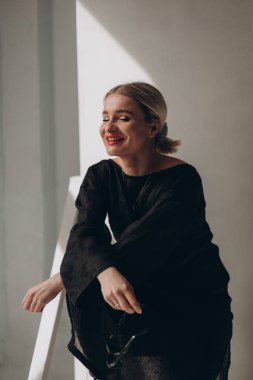 Siyah bir sokakta şık bir kadın, güneş ışığında poz veren gözlüklü.