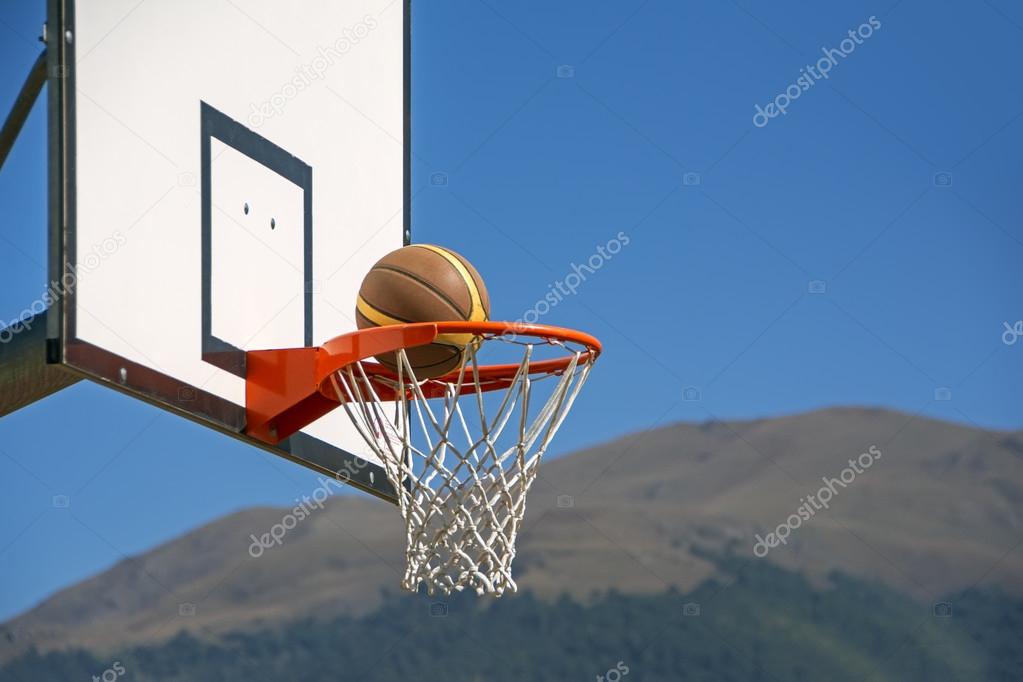 Basketball backboard against a clear blue sky with ball going through hoop