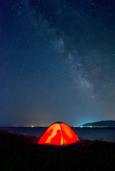 orange tent with tourists on the shore of Lake Sevan under the Milky Way