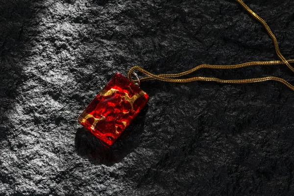 Red pendant with gold chain a black granite surface