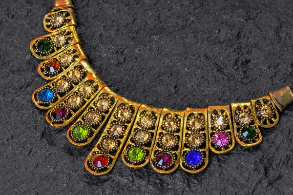 Collar de oro con piedras de colores sobre una superficie de granito negro —  Fotos de Stock