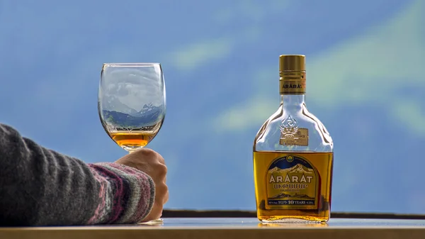 Beatenberg, Szwajcaria - 14 czerwca 2015: Butelka słynnej ormiański koniak Ararat 10 lat i szkło na tle Alpy Szwajcarskie — Zdjęcie stockowe