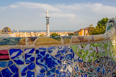 Barselona, İspanya - 31 Temmuz 2019: Antonio Gaudi 'nin güzel mozaik kürsüsünün yakın çekimi Park Guell' in ikonik kulesi ve bulanık arka planda şehir. Sığ alan derinliği
