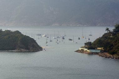 Uzak lüks yatlar ve dağlardaki deniz suyunda yüzen yelkenliler günbatımı ışıklarıyla aydınlanan bulanık bir arka plan. Hong Kong, Çin 'deki Repulse Bay Yolu' ndan Derin Su Koyu manzaralı.