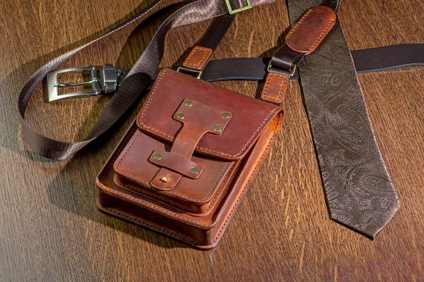 Mens brown accessories - leather bag, belt and paisley pattern brown tie on wooden table background