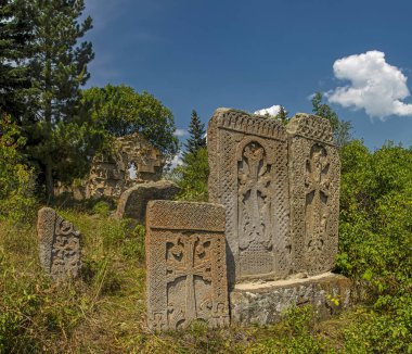 Ermenistan 'ın Artavaz köyündeki yeşil ağaçların üzerinde geleneksel Ermeni haçkarları (çapraz taş) ve mavi gökyüzü bulunan antik Artavazavank Manastırı (7. yüzyıl) panoraması