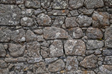 Çimento çatlakları ve güneş ışığıyla aydınlatılan kayaların üzerindeki liken ile taştan duvar yüzeyinin gri arkaplan dokusu