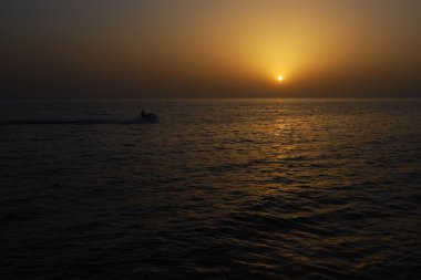 adam bir Jet Ski yarışları günbatımı, dalgalar aracılığıyla