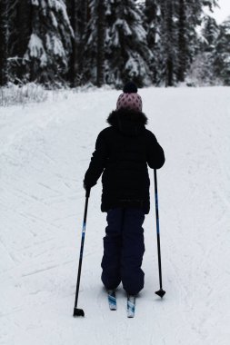 Küçük kız kış ormanında kayak yapıyor.
