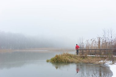Kırmızı kazaklı adam sisli kış gününde nehirde iskelede.