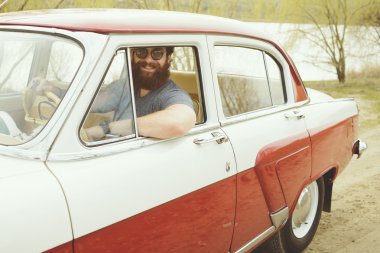 Retro bir arabanın direksiyonuna sakallı adam