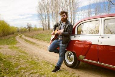Sakallı adam açık havada retro car yakınındaki gitar çalmak