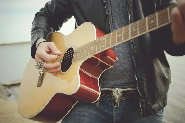 Bearded man playing guitar outdoors near retro car