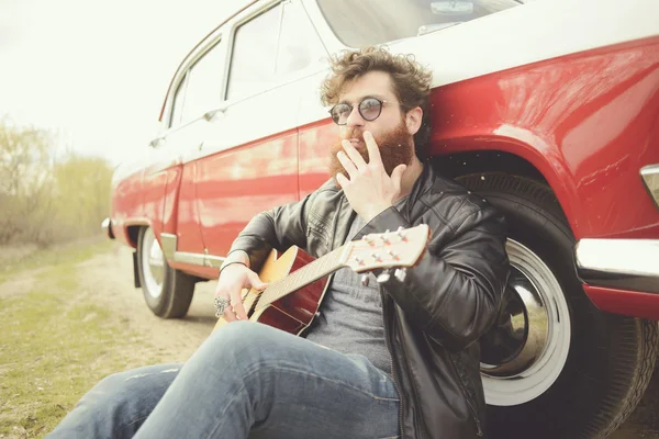 Barbudo hombre tocando la guitarra al aire libre cerca de coche retro — Foto de Stock