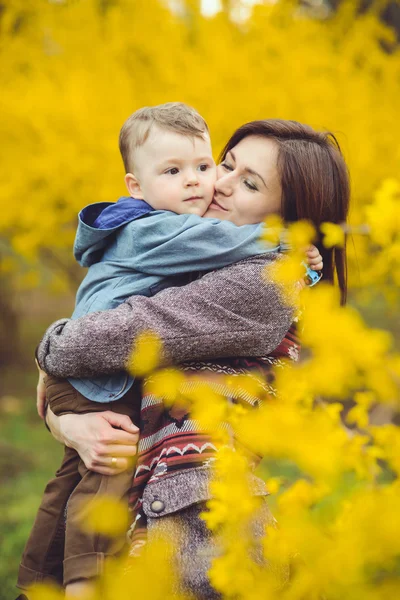 Mother and son happy in the park, near yellow flowers — Stock Photo, Image
