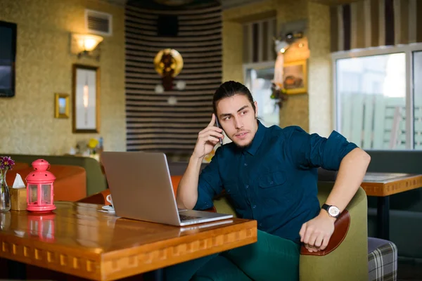 Молодой человек пьет кофе и работает на ноутбуке в кафе — стоковое фото