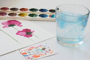 Pembe manolya çiçeğinin suluboya resmi ve beyaz masada sanatsal aletler. Sanatsal işyerinin natürmort yaşam bileşimi