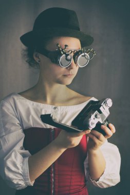 Gözlük ve şapka takan çekici steampunk kızı, eski kamerayı tut.