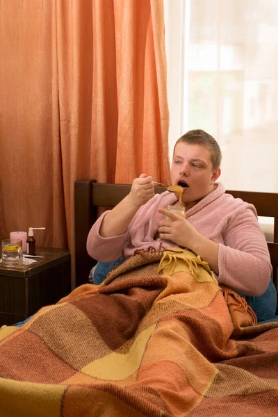 Άρρωστος Μπουρνούζι Ξαπλωμένος Στο Κρεβάτι Και Τρώγοντας Μέλι — Φωτογραφία Αρχείου