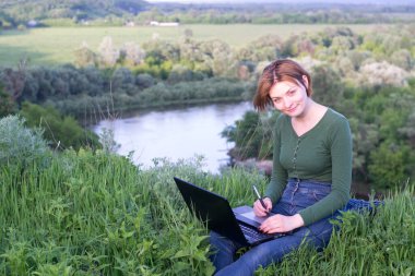 Güzel kız çimlerin üzerinde otururken grafik tabletini kullanıyor.
