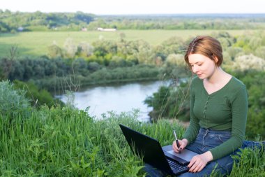 Güzel kız çimlerin üzerinde otururken grafik tabletini kullanıyor.